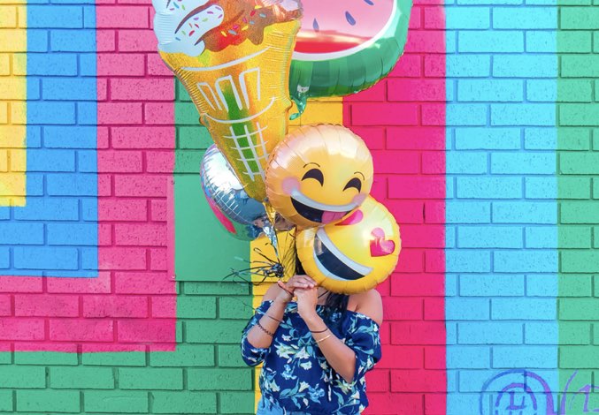 Girl holding emoji balloons in front of her face